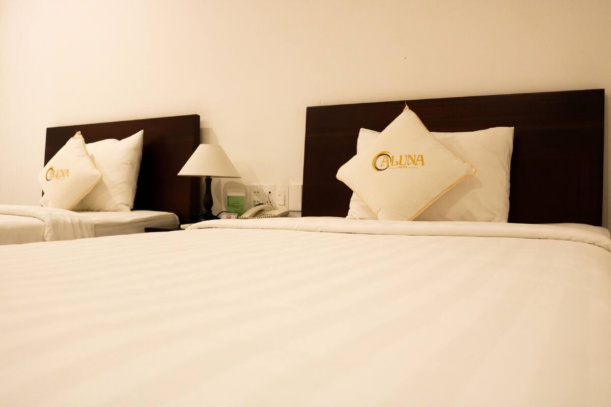 Habitación de hotel con dos camas, cada una con cabecera y almohadas que muestran el nombre del hotel.