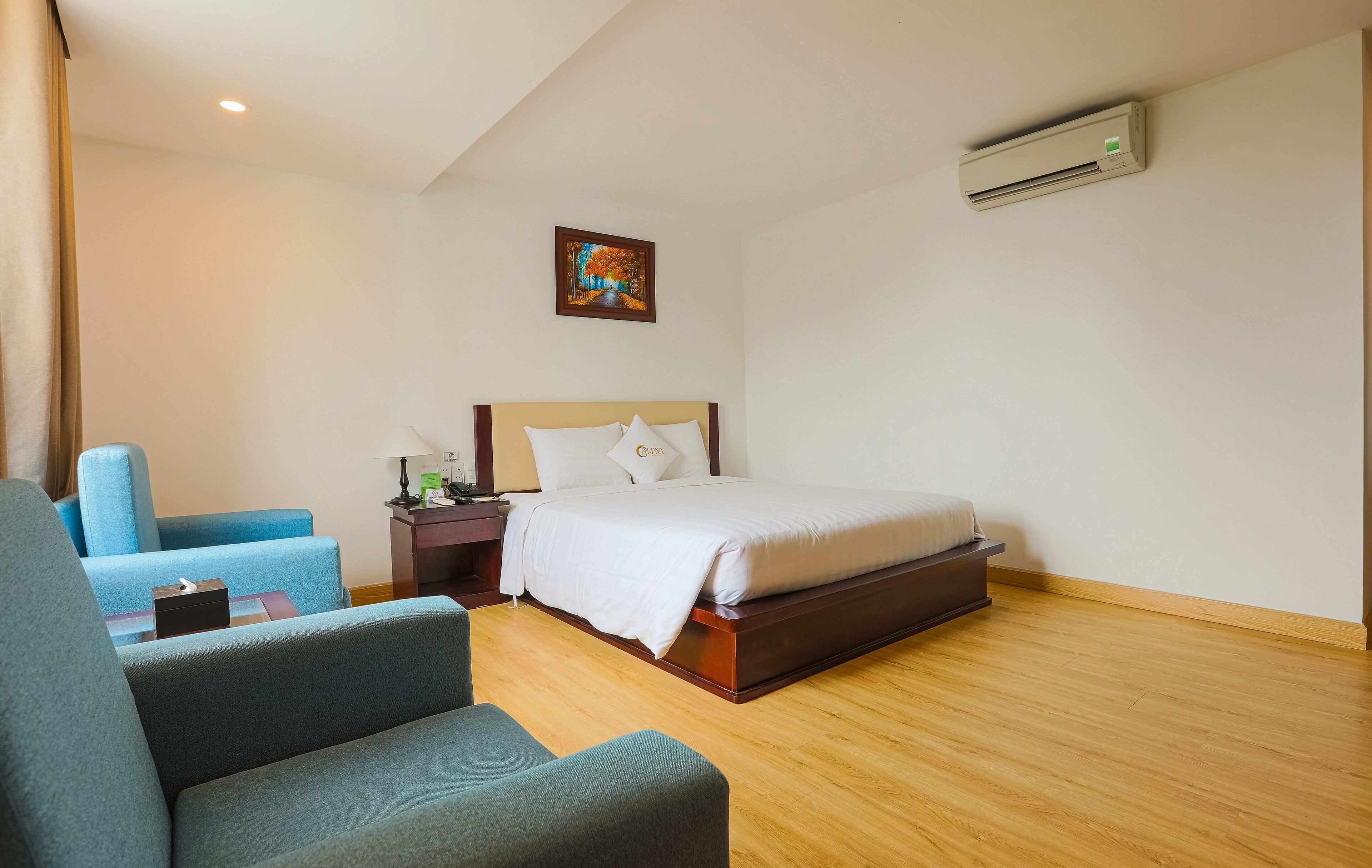 Een hotelkamer met een bed, een stoel, een nachtkastje, een airconditioner en een schilderij aan de muur.