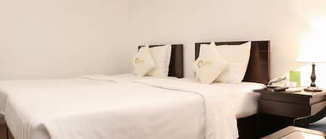 A hotel room with a large bed, two pillows with a logo, a bedside table with a lamp, and a small table with a phone and a notepad.