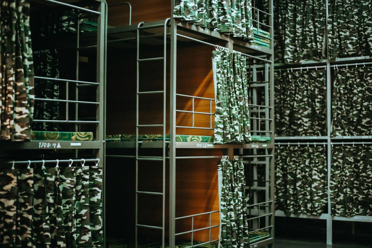 Bunk beds with camouflage curtains and metal shelves in a storage area.