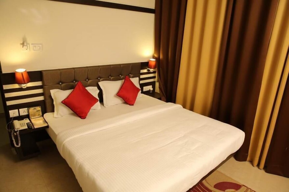 A hotel room with a large bed, two red pillows, a white bedspread, a nightstand with a telephone, and a wall-mounted light fixture.