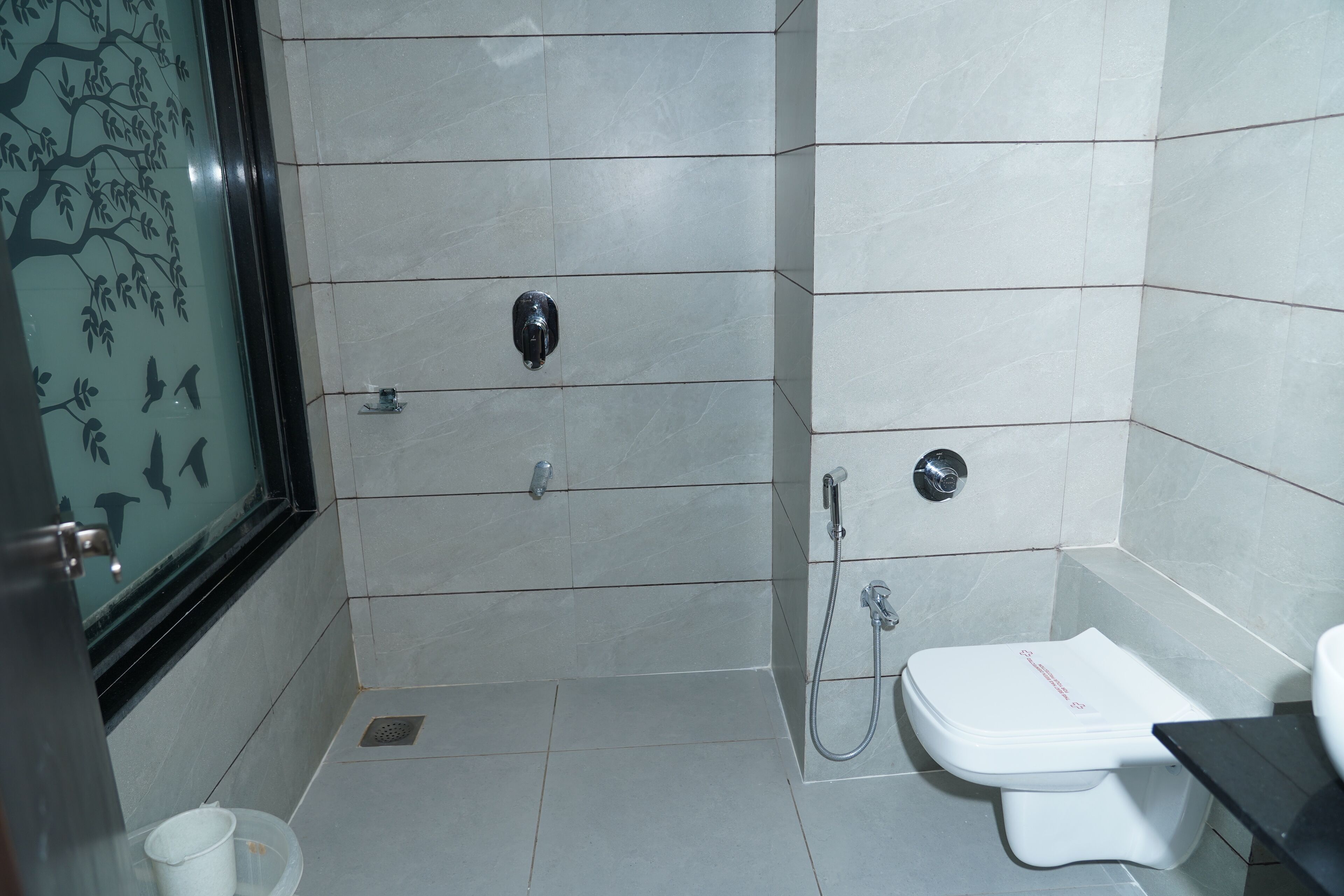 A bathroom with a shower, toilet, and a window with a tree design.