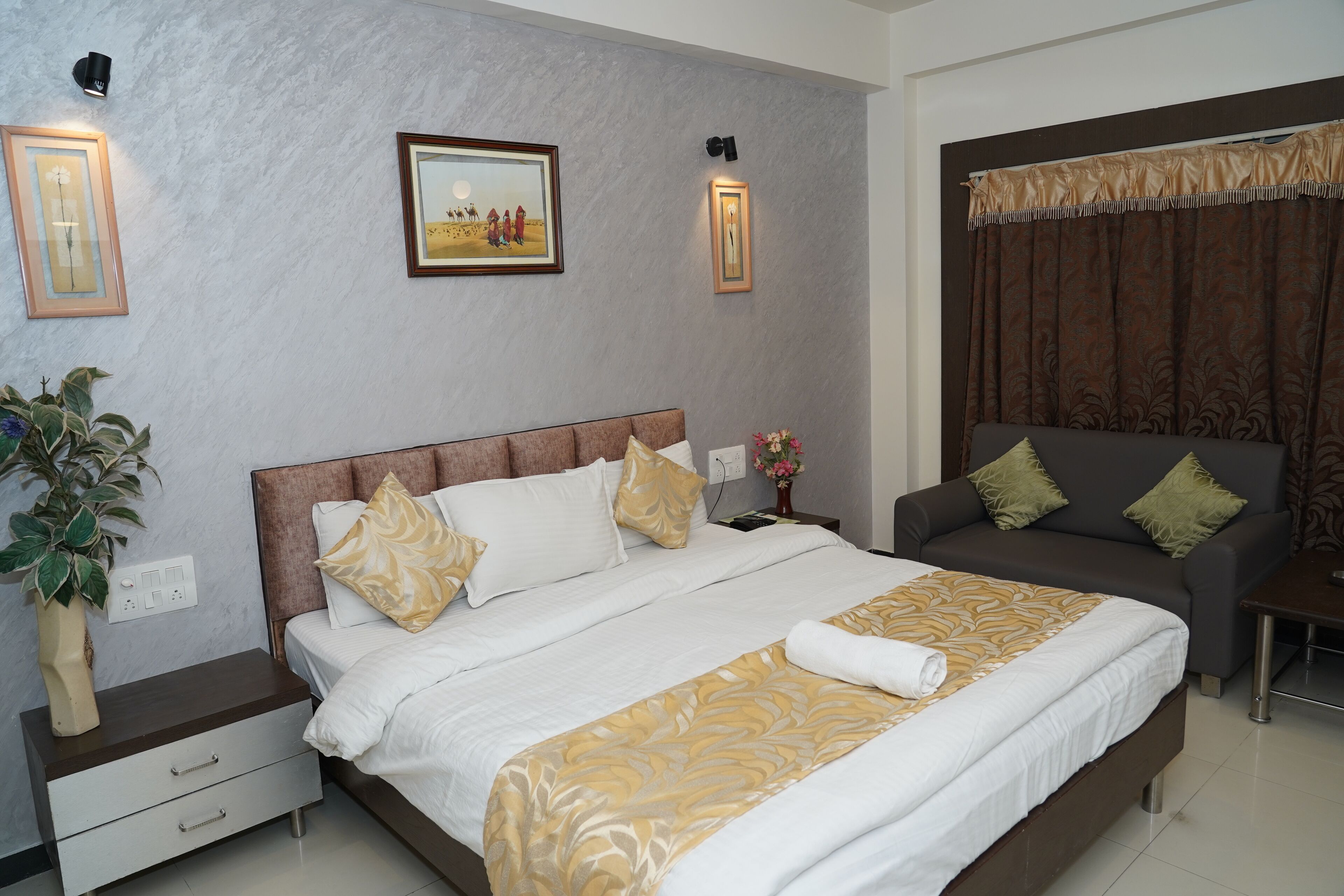A hotel room with a large bed, a sofa, a nightstand, a lamp, and a wall-mounted picture.