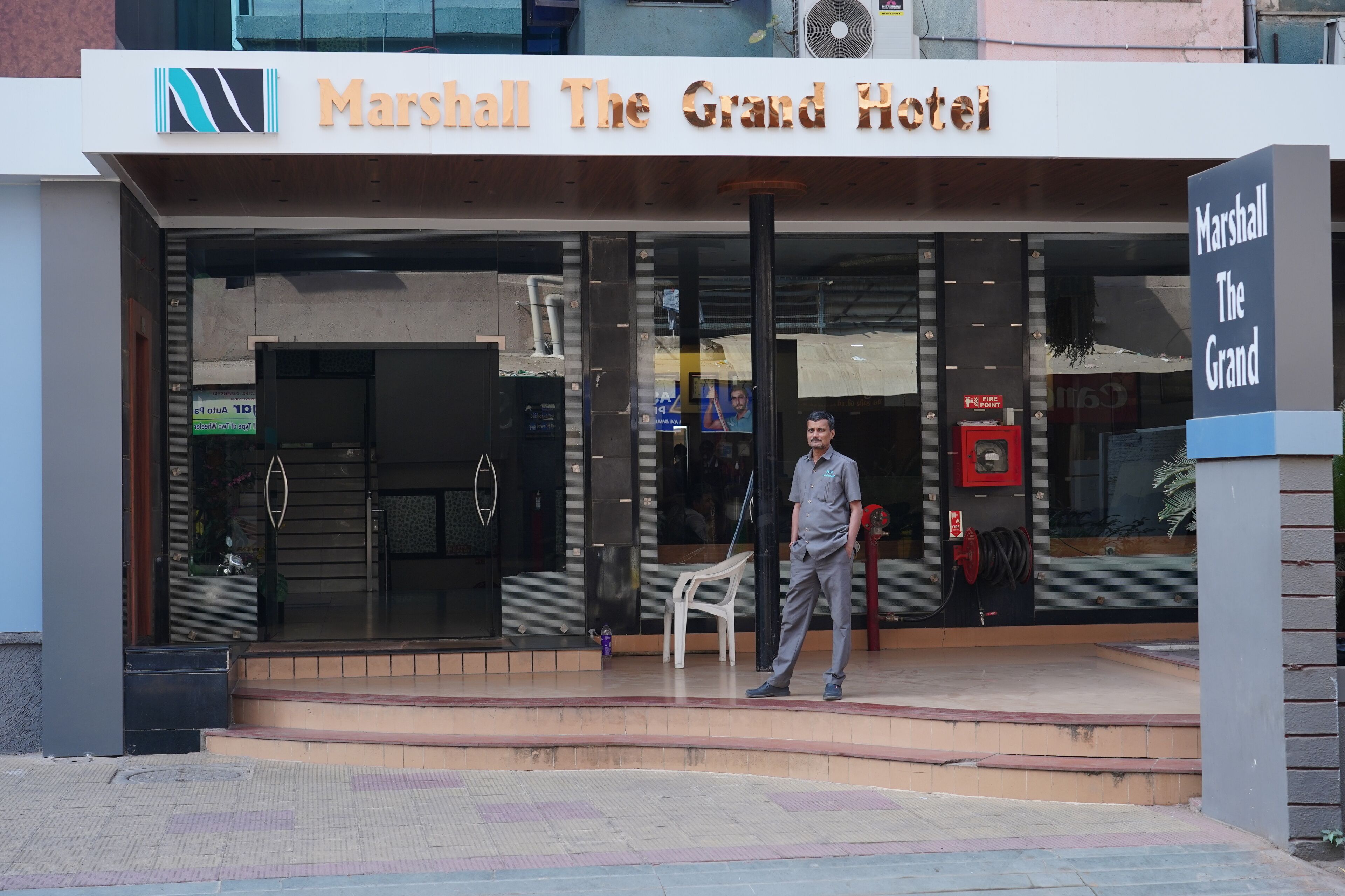 The exterior of Marshall The Grand Hotel with a clear entrance, a signboard, and a man standing in front.