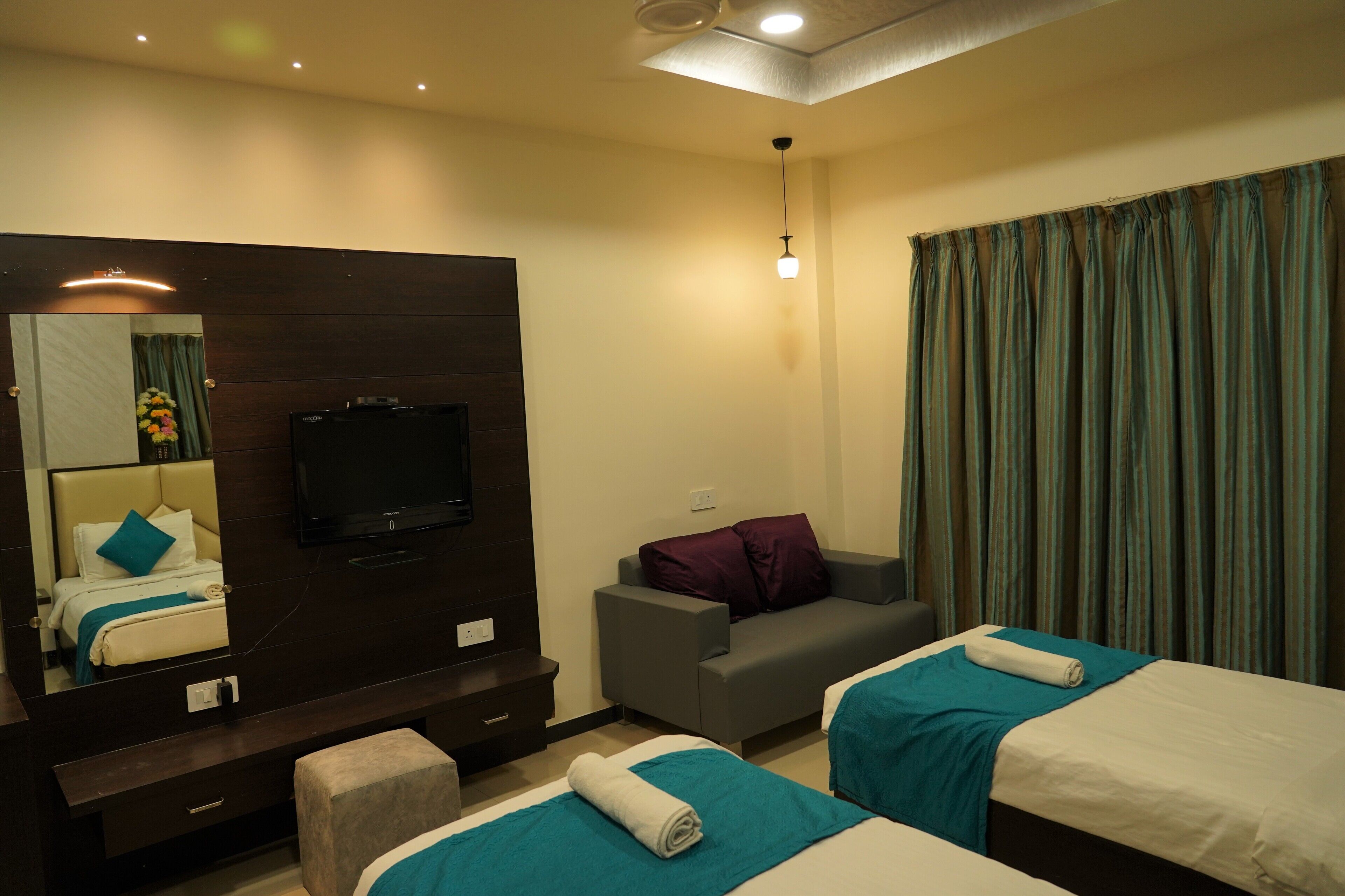 A hotel room with two beds, a TV, a sofa, and a large mirror.