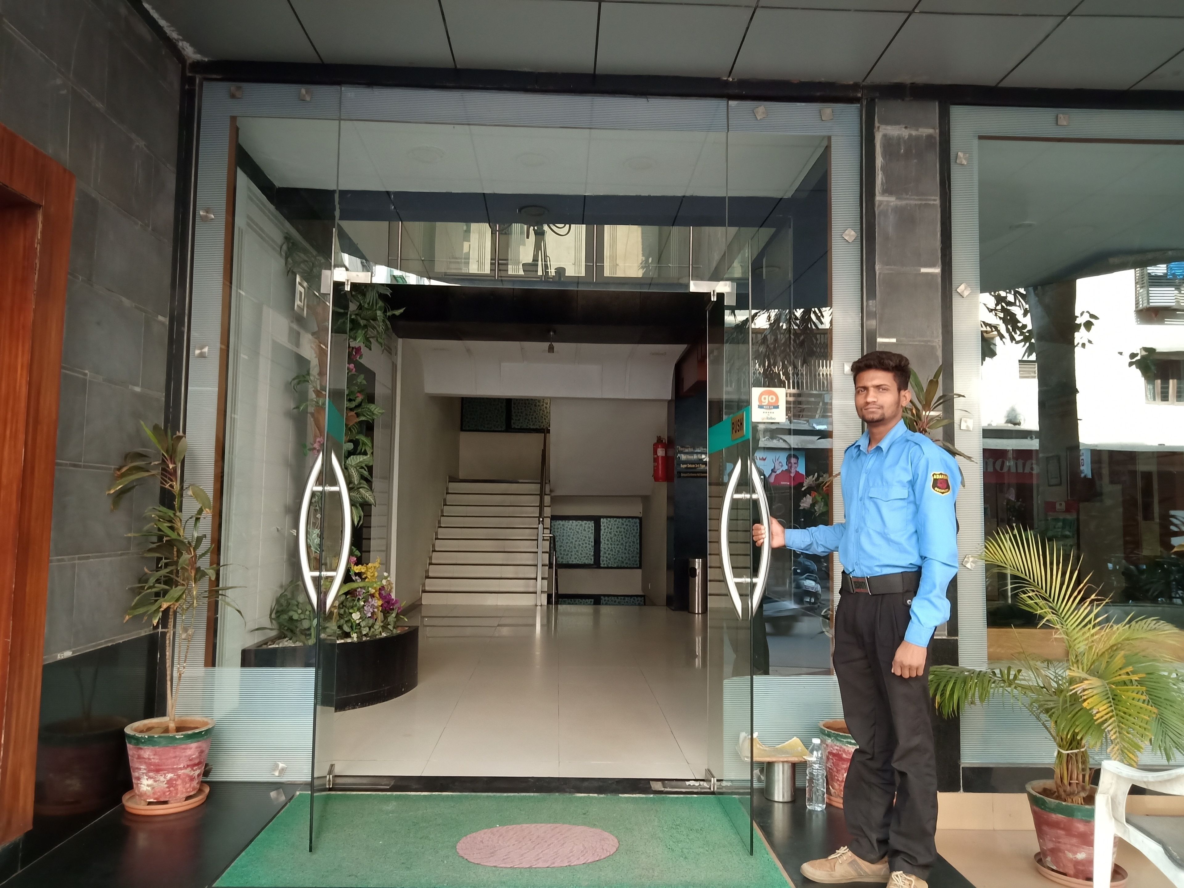 A hotel entrance with a glass door, a staircase inside, and potted plants outside.