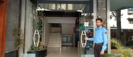 A hotel entrance with a glass door, a staircase inside, and potted plants outside.