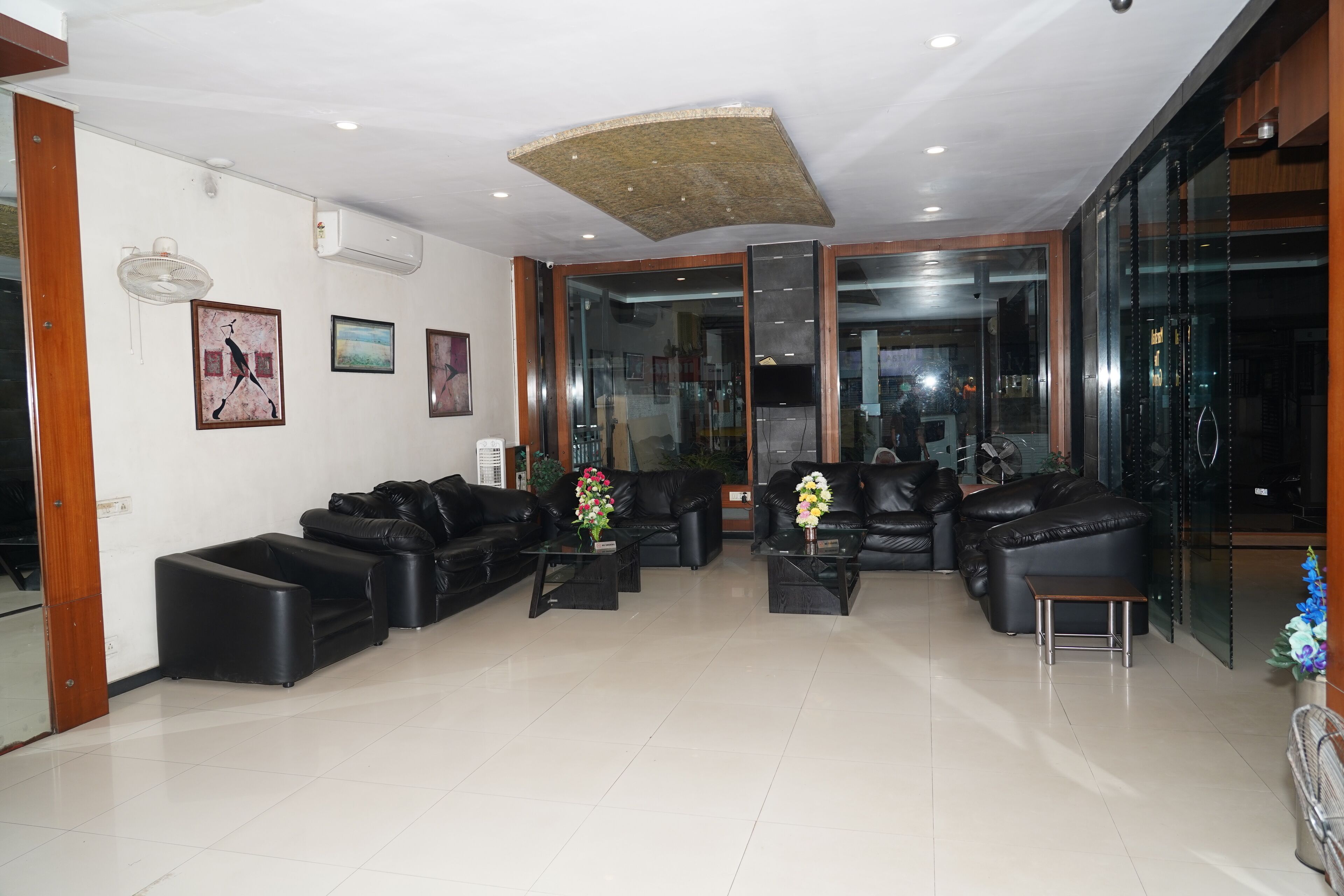 A spacious lobby with black leather sofas, a glass wall, and a ceiling fan.