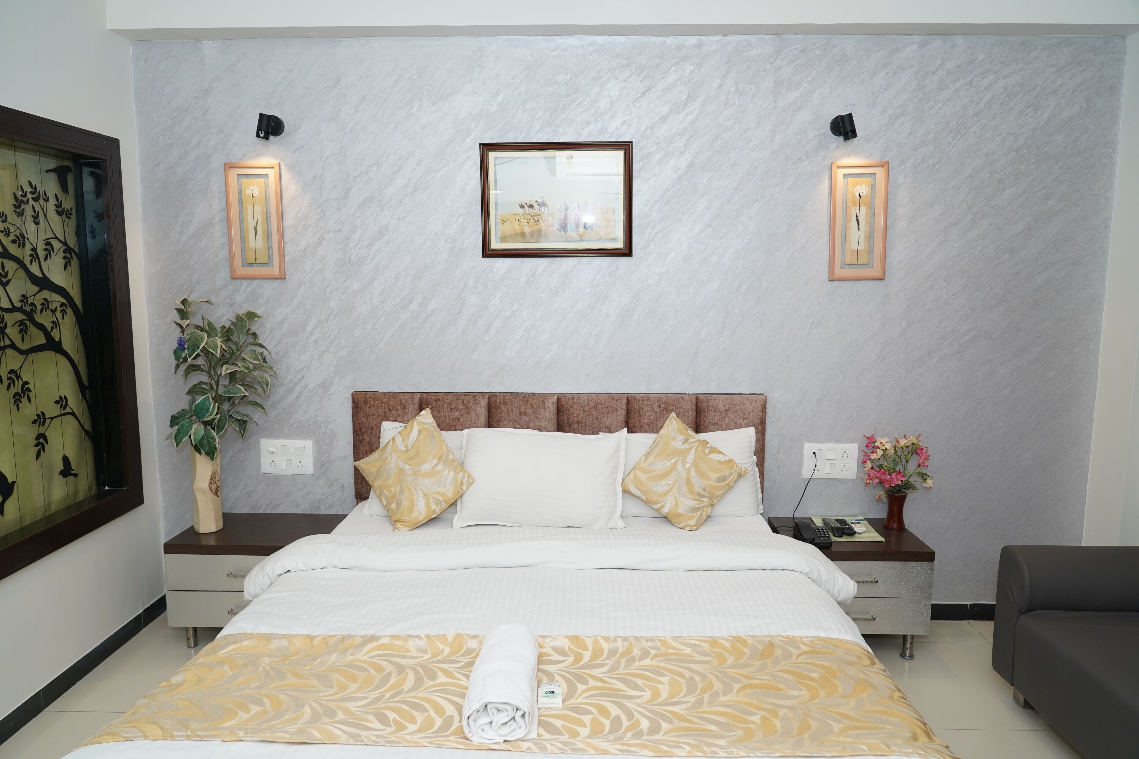 A neatly arranged hotel room with a bed, bedside tables, a nightstand, a sofa, and a wall-mounted mirror.