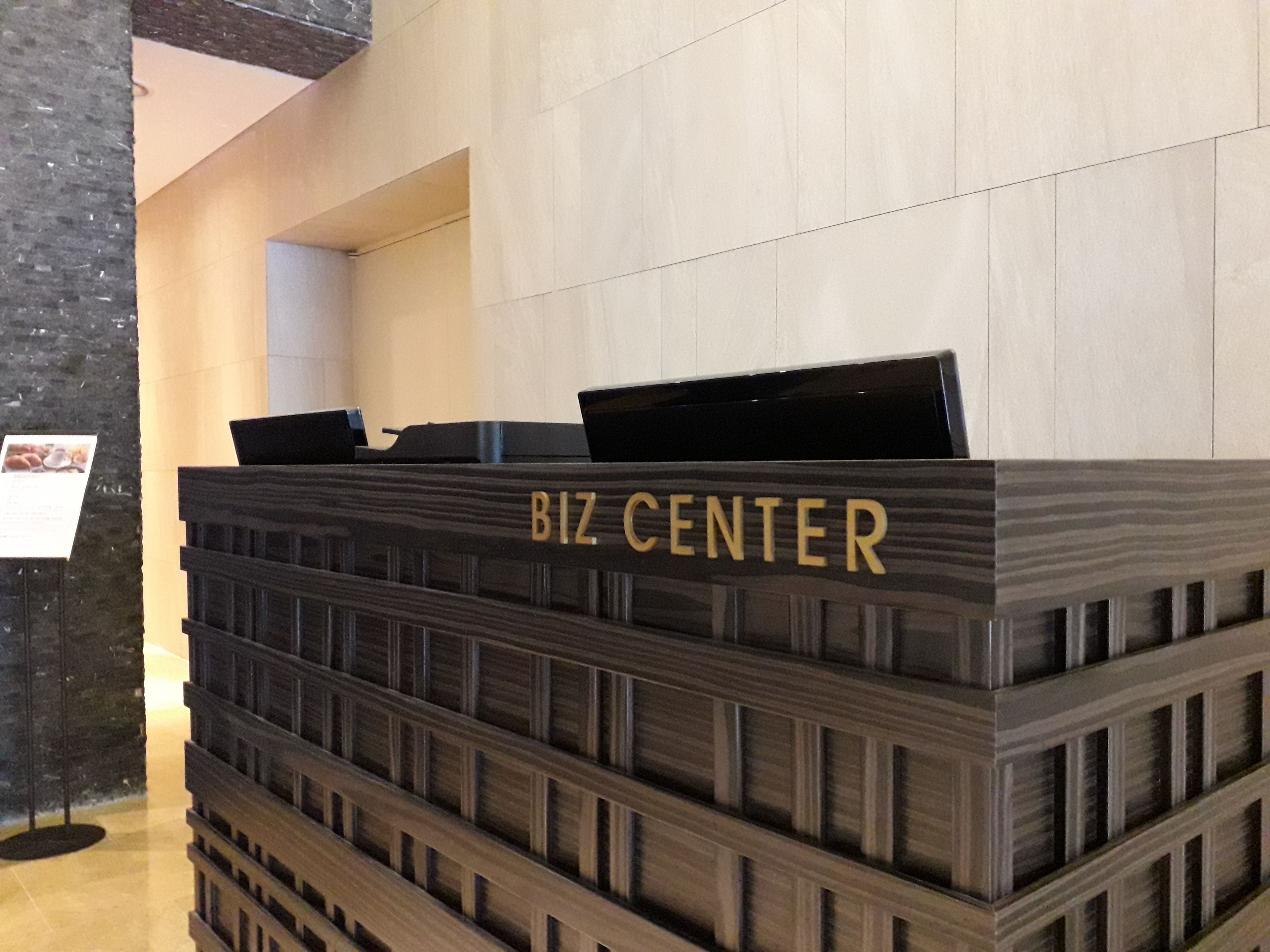Un mostrador de recepción con el rótulo 'BIZ CENTER', diseño moderno, superficie plana y una pequeña zona de exhibición.