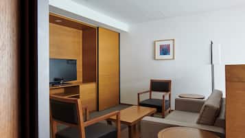 Un hotel moderno con un armario de madera, un televisor de pantalla plana, un sofá, dos sillones, una mesita y un cuadro en la pared.