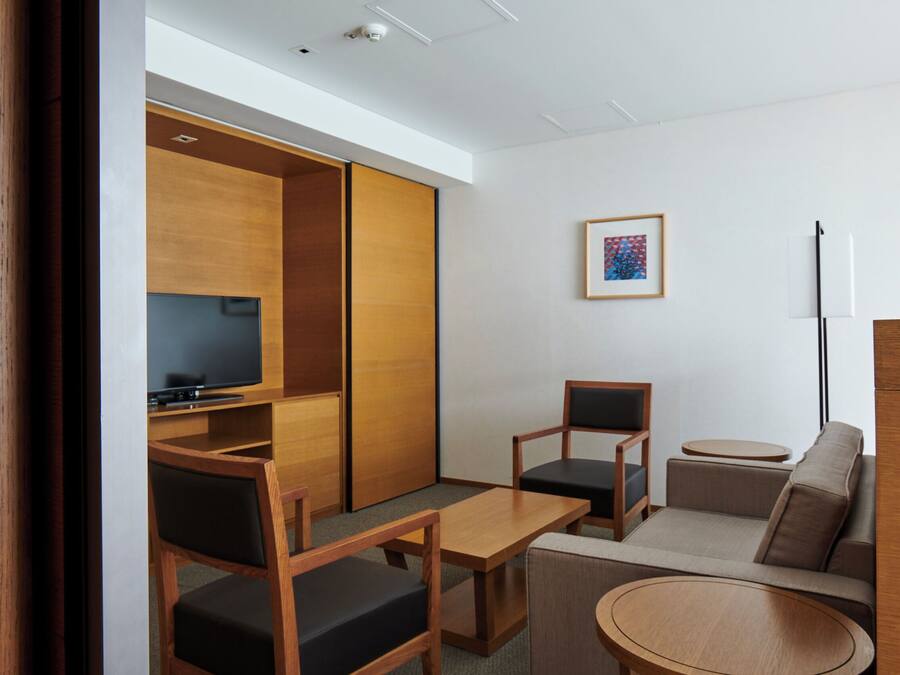 Un hotel moderno con un armario de madera, un televisor de pantalla plana, un sofá, dos sillones, una mesita y un cuadro en la pared.