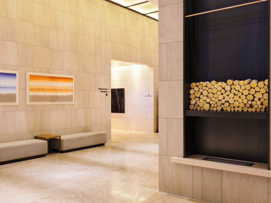 A modern hotel lobby with a reception desk, seating area, and a fireplace with wood logs.