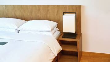 A neatly made bed with white linens and pillows, a wooden headboard, and a bedside table with a lamp.
