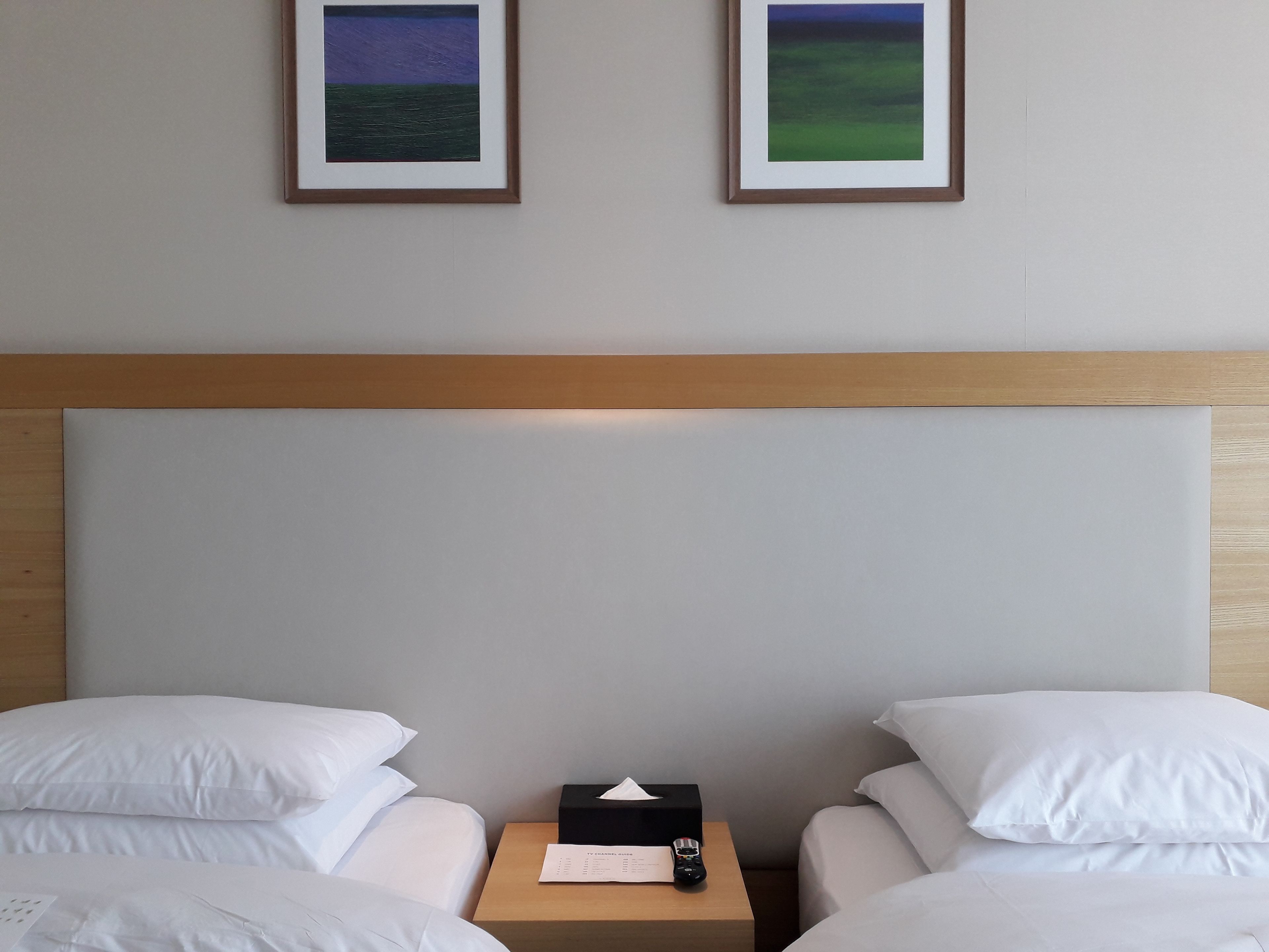 A hotel room with two beds, a wooden headboard, and two framed pictures on the wall.