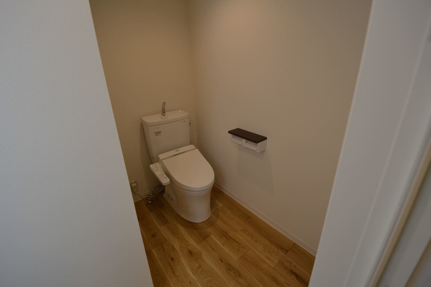 Un baño pequeño y estrecho con inodoro, piso de madera y pared blanca.