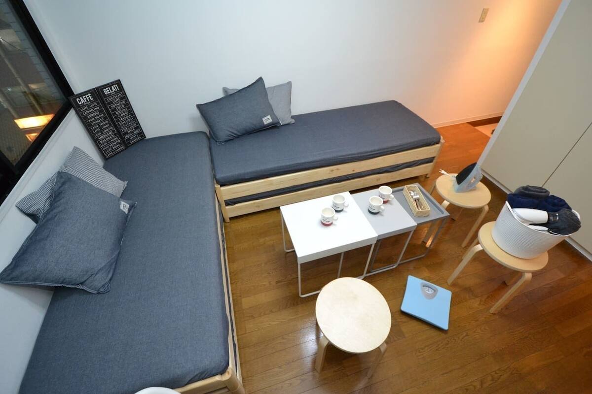 A compact room with a sofa bed, a small table with cups, a laptop, and a chair.