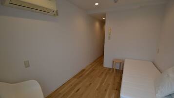 A small, sparsely furnished room with a wooden floor, a single bed, a small stool, and a white chair.