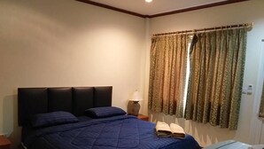 A bedroom with a large bed, a bedside table with a lamp, and a window with curtains. - Ponderosa Resort (Pattaya)