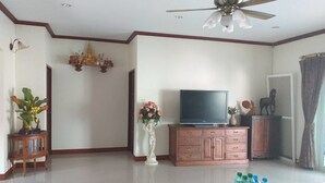 A living room with a television, a cabinet, decorative items, and a ceiling fan. - Ponderosa Resort (Pattaya)