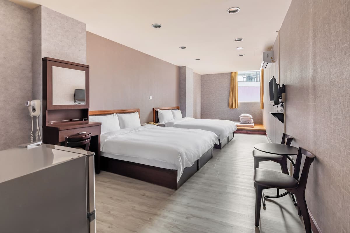 A hotel room with two beds, a desk, a chair, a TV, and a minibar.