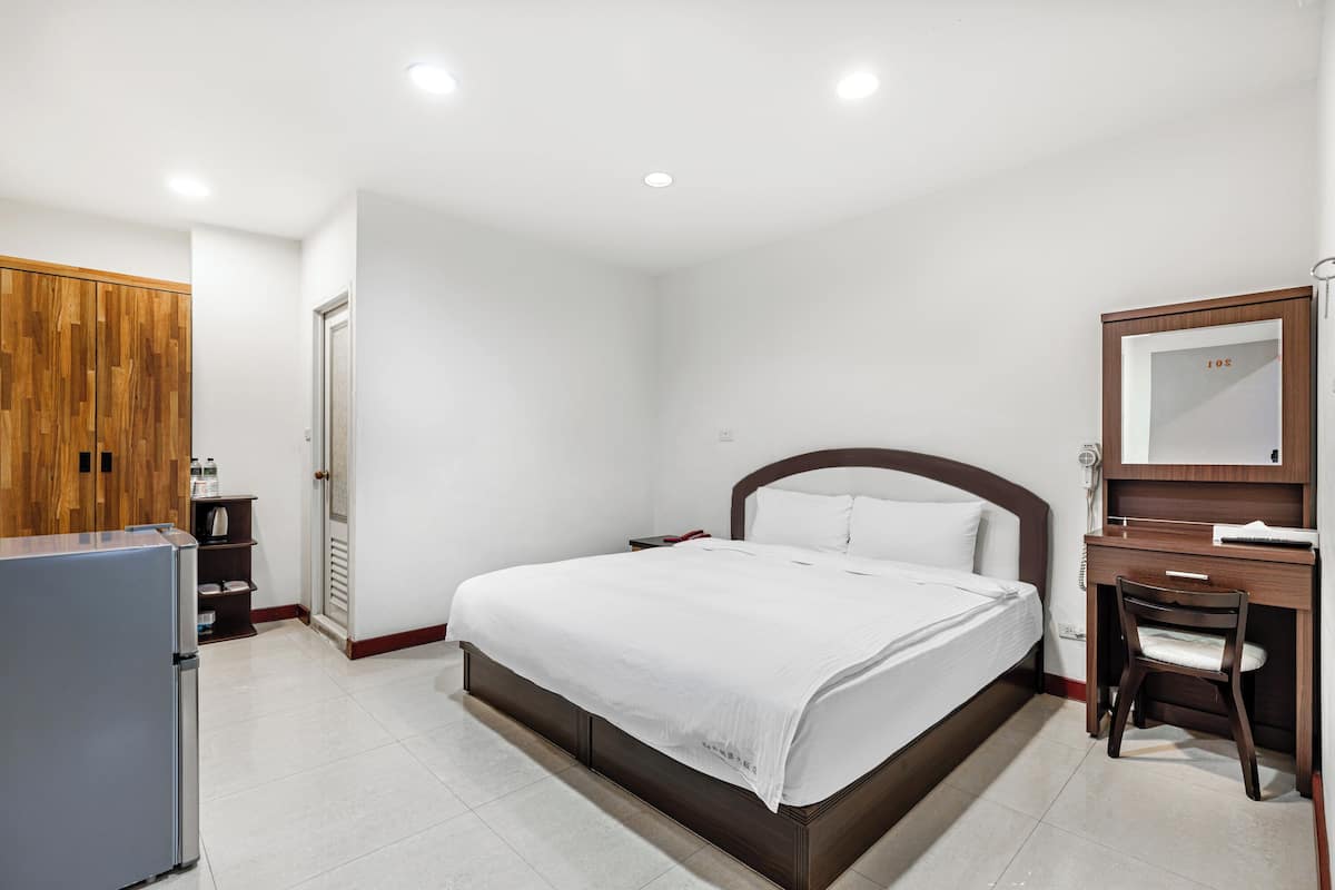 A bedroom with a bed, a desk, a chair, a wardrobe, and a refrigerator.