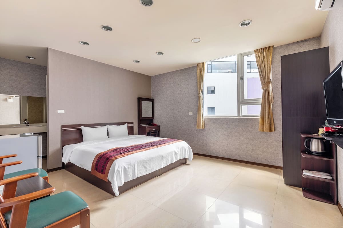 A hotel room with a bed, a desk, a chair, a TV, a wardrobe, and a window with curtains.