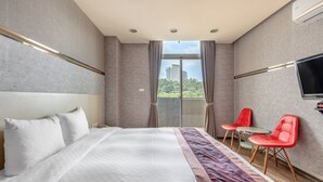 Una habitación de hotel moderna con una cama grande, un televisor montado en la pared y un balcón con sillas rojas.