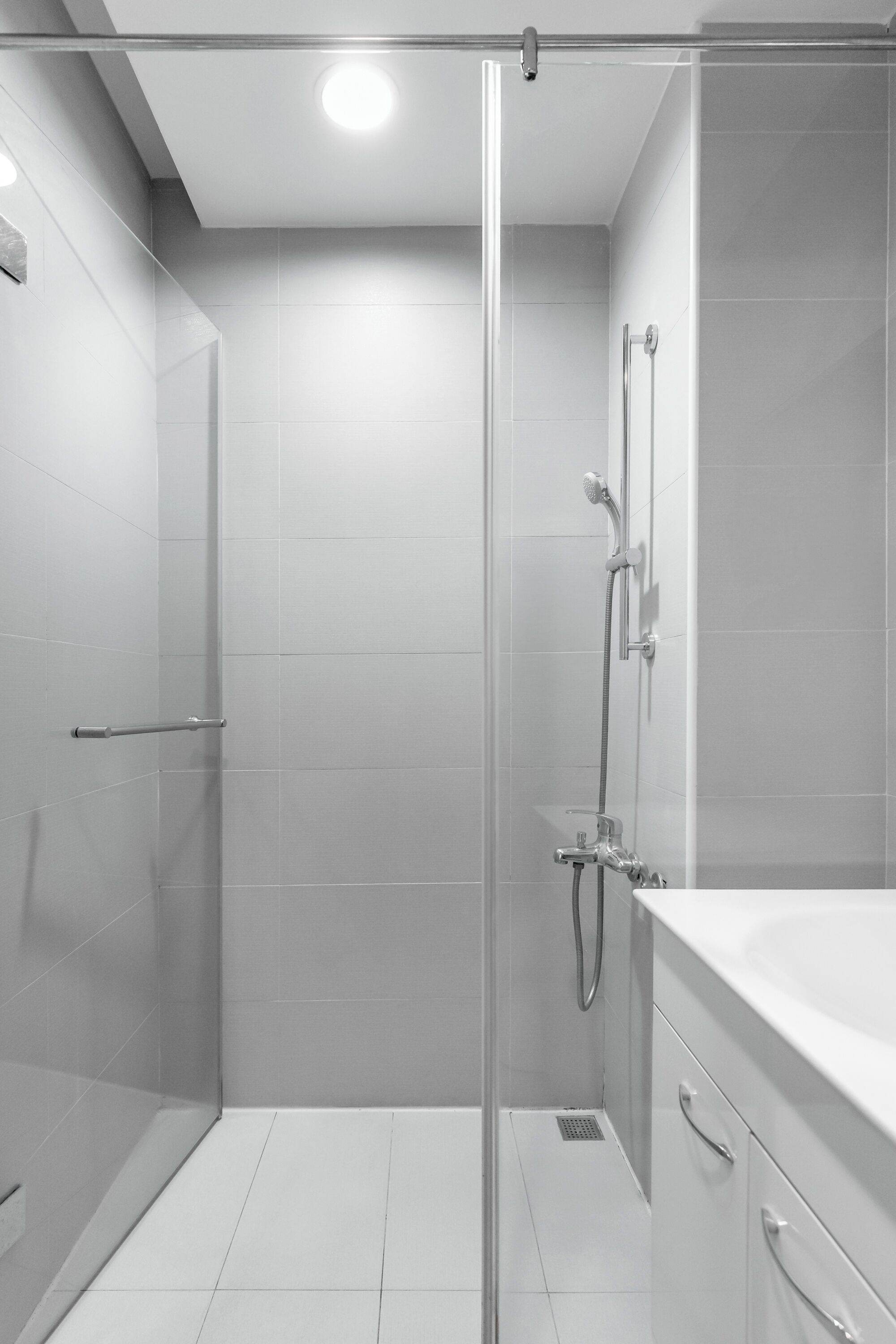 Ein modernes Badezimmer mit einer Duschkabine aus Glas, einem weißen Waschbecken und einem gefliesten Boden.