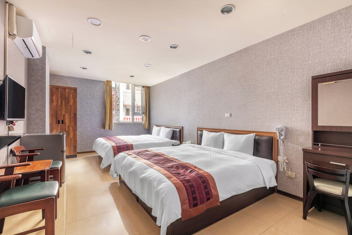 A hotel room with two beds, a desk, a chair, a TV, and a window with curtains.