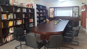 A conference room with a long table, black chairs, and bookshelves filled with books and decorative items. - Persatuan Kebajikan Sri Sakthi Ashram - Hostel (Tangkak)