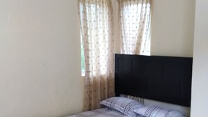 A bedroom with a wooden floor, a bed with a black headboard, and two windows with sheer curtains. - Persatuan Kebajikan Sri Sakthi Ashram - Hostel (Tangkak)