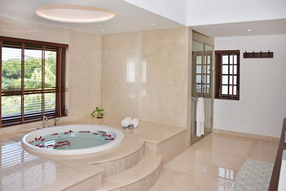 Une salle de bain moderne avec une grande baignoire, une douche à l’italienne en verre et une vue sur la verdure.