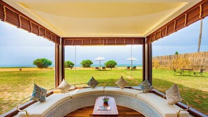 Ein gebogenes Sitzarrangement mit Tisch, mit Blick auf einen grünen Außenbereich mit Sonnenschirmen und Stühlen.