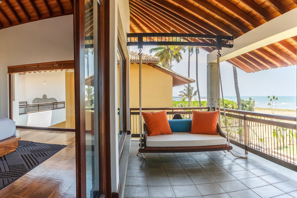 A bedroom with a bed, a balcony with a swing, and a view of the ocean.