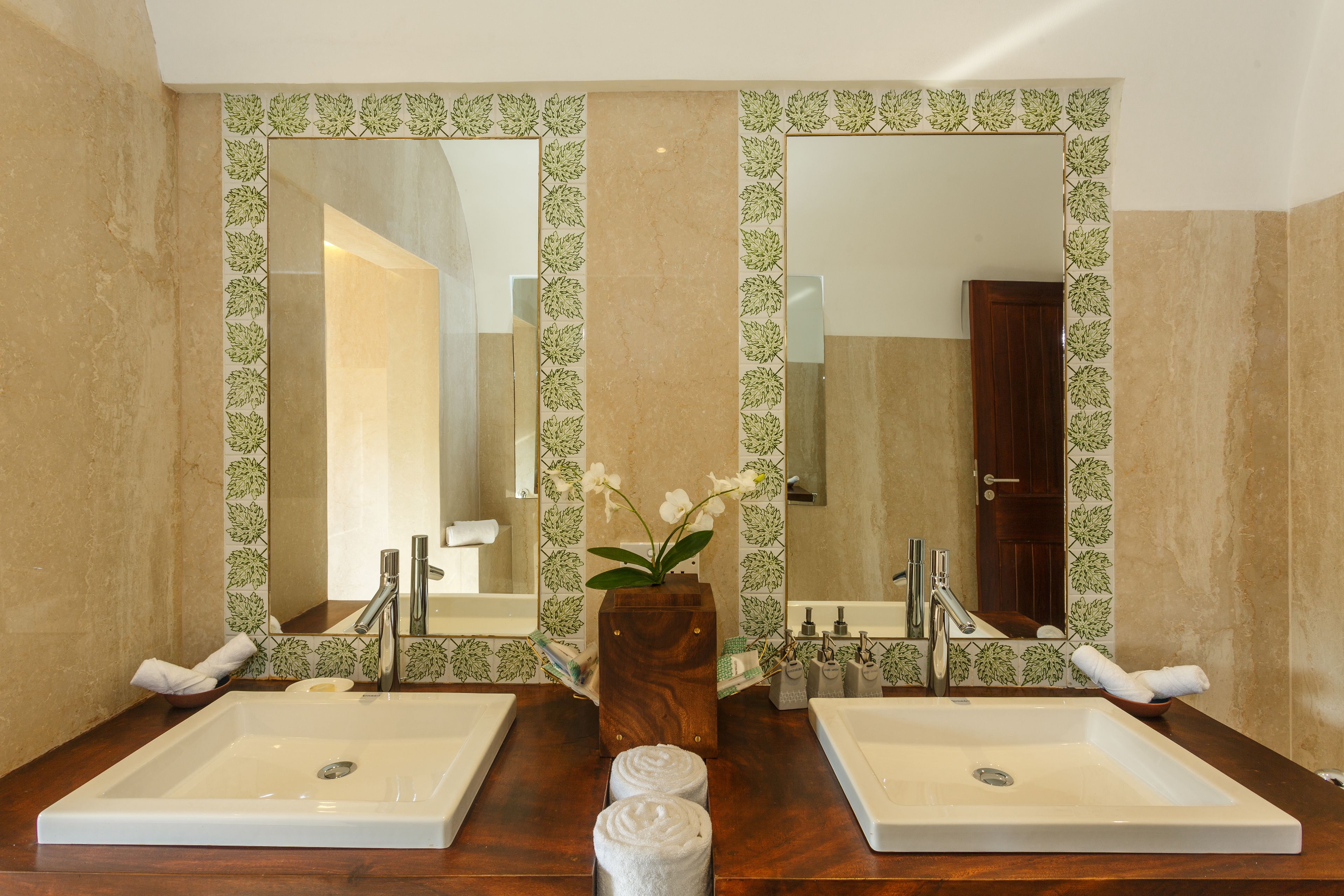 A bathroom with two sinks, a mirror, and a vase with flowers.
