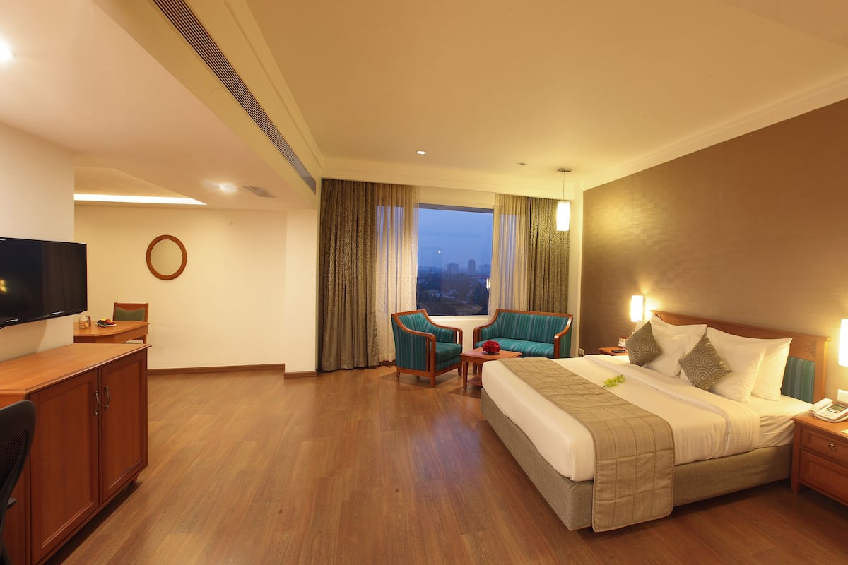 Habitación de hotel con cama, escritorio, televisión, silla, mesa y vista a la ciudad.