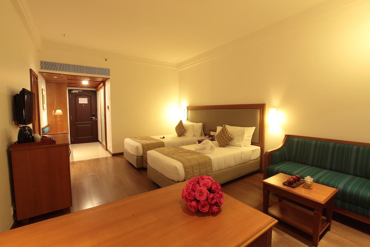 Una habitación de hotel con dos camas, un sofá, una mesa de madera con un ramo de rosas rojas y un televisor sobre un mueble de madera.