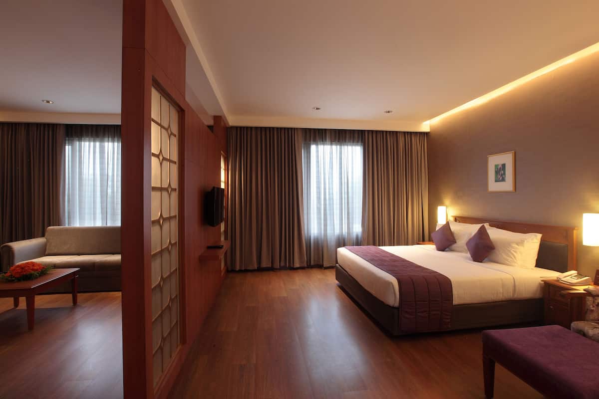 Una habitación de hotel con una cama grande, un sofá, piso de madera y un televisor montado en la pared.