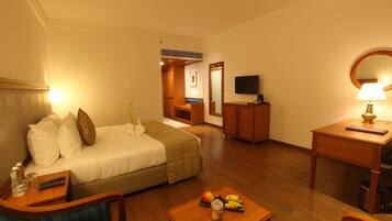 A hotel room with a bed, a desk, a chair, a TV, and a lamp.