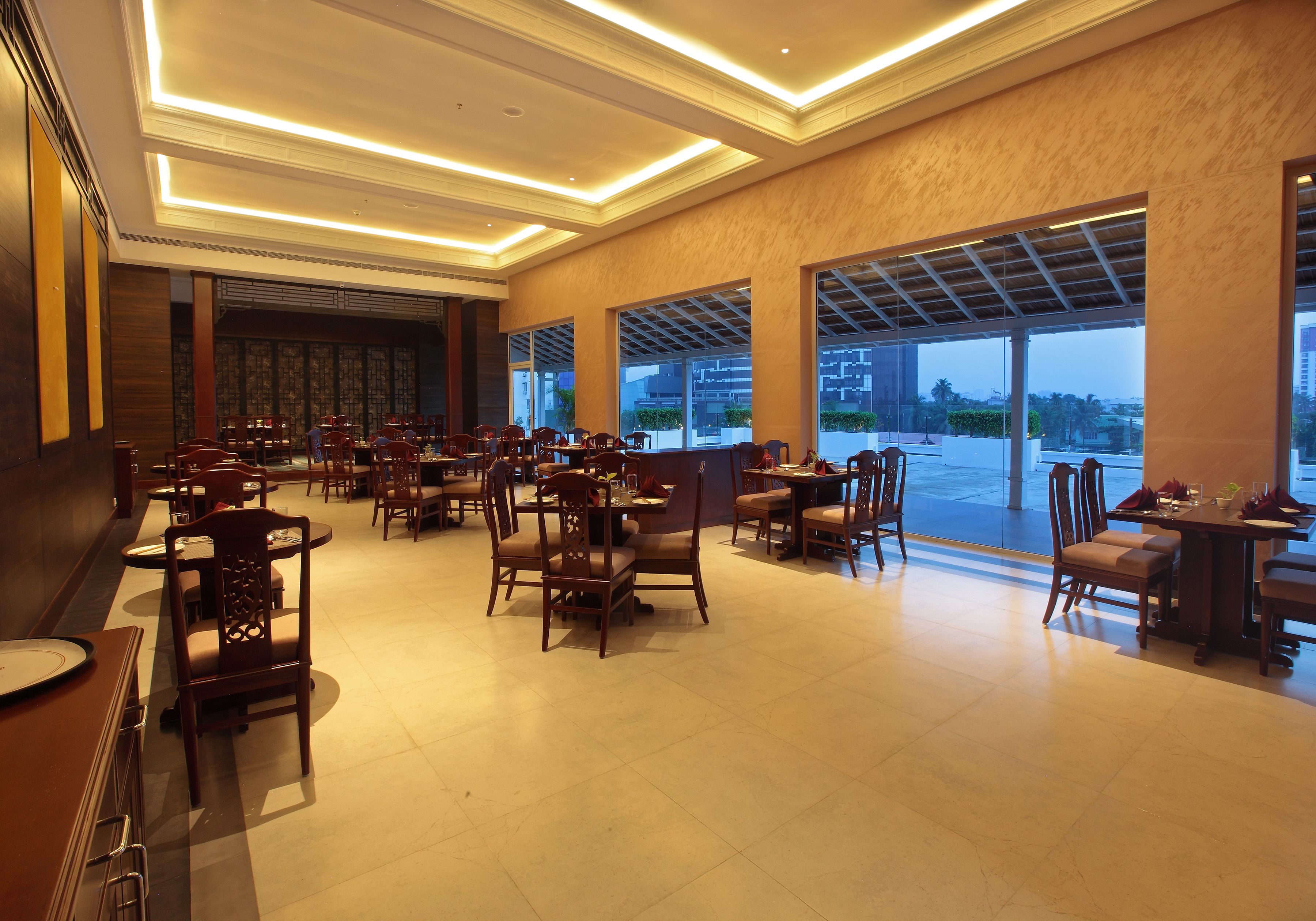 Un restaurante amplio con varias mesas y sillas, ventanas grandes y un diseño de techo moderno.