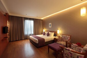 A hotel room with a large bed, a wooden nightstand, a chair, and a television on the wall.