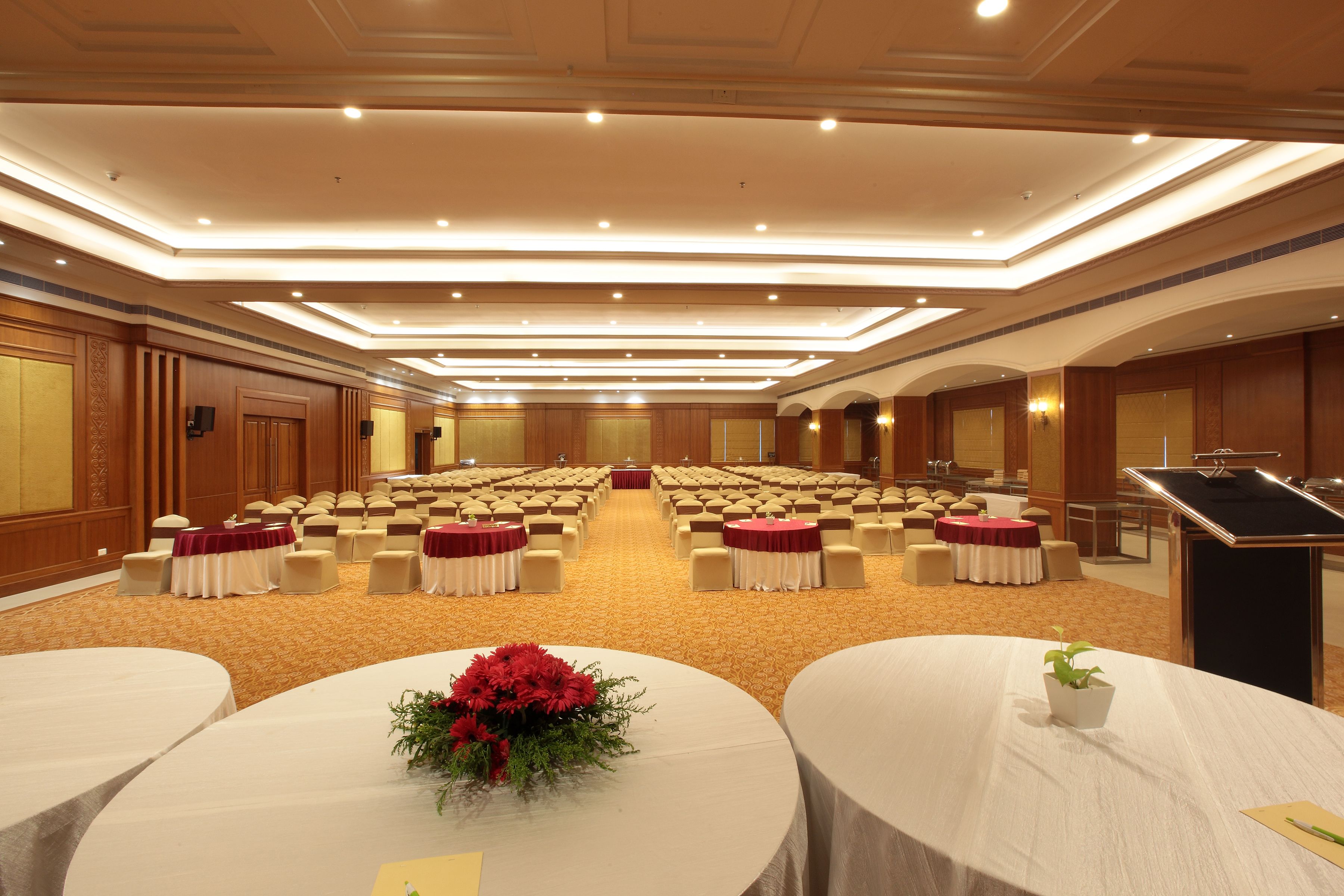 Un salón de conferencias con filas de sillas, un atril y mesas decoradas con centros de flores.