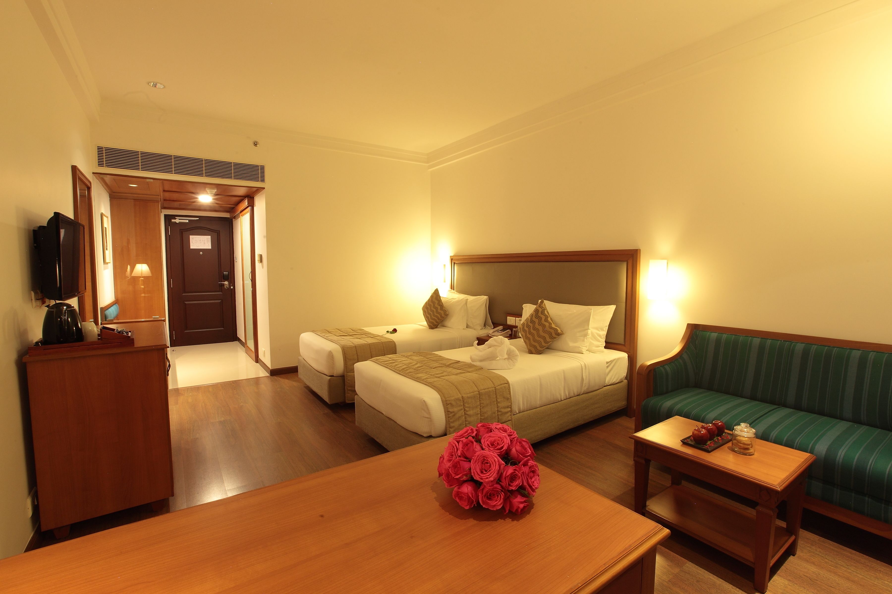 A hotel room with two beds, a sofa, a wooden table with a bouquet of flowers, and a television on a desk.