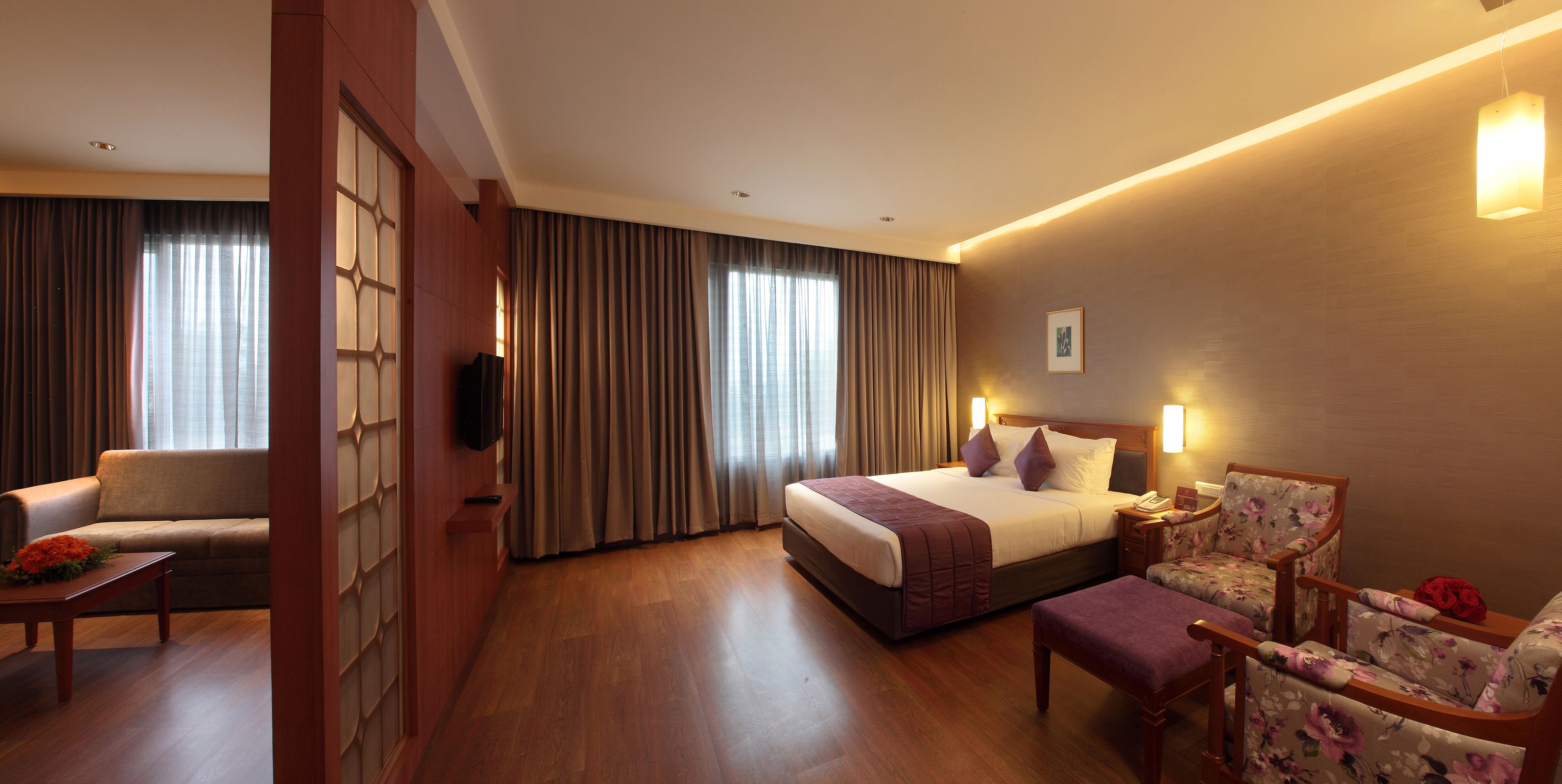 A hotel room with a bed, a sofa, a chair, a small table, and a TV.