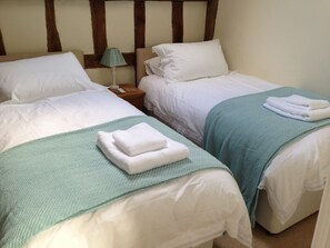 Two single beds with white linens, a green throw blanket on one bed, and a lamp on a bedside table. - 15th Century Period Cottage In Saffron Walden, Essex England (Saffron Walden)