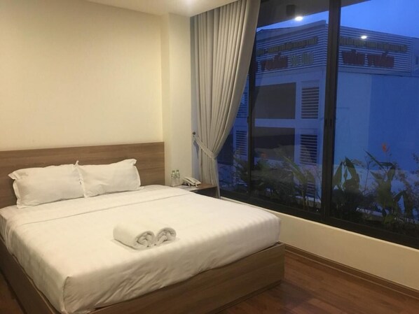 Habitación de hotel con una cama grande, una mesita de noche, una ventana con cortinas y vistas a un edificio.