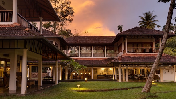 A resort with multiple buildings, outdoor seating areas, and a well-maintained lawn. - Cranganor History Cafe Riverside Chateau (North Paravur)