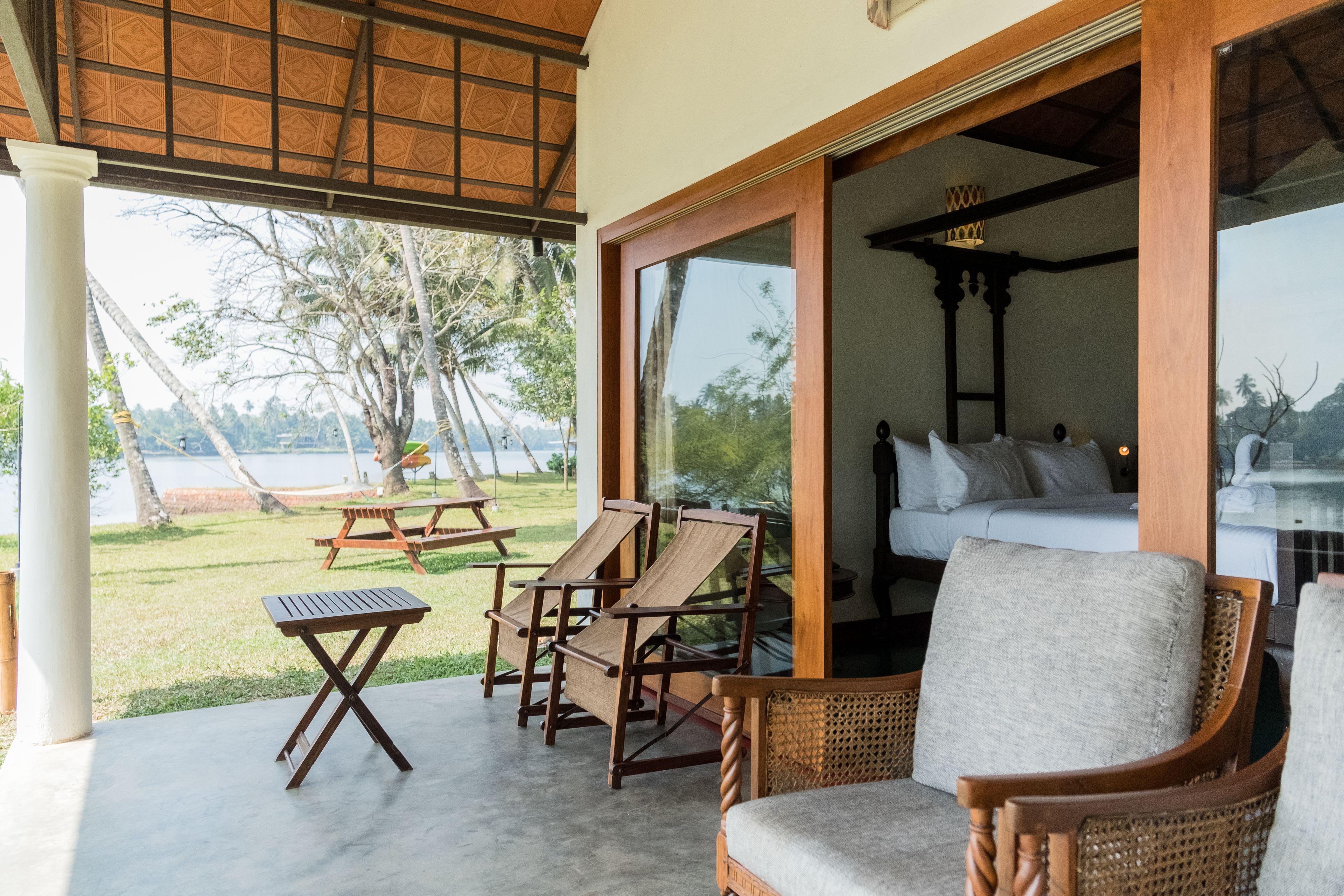 A room with a bed, a wooden chair, a small table, and a view of the outdoors.