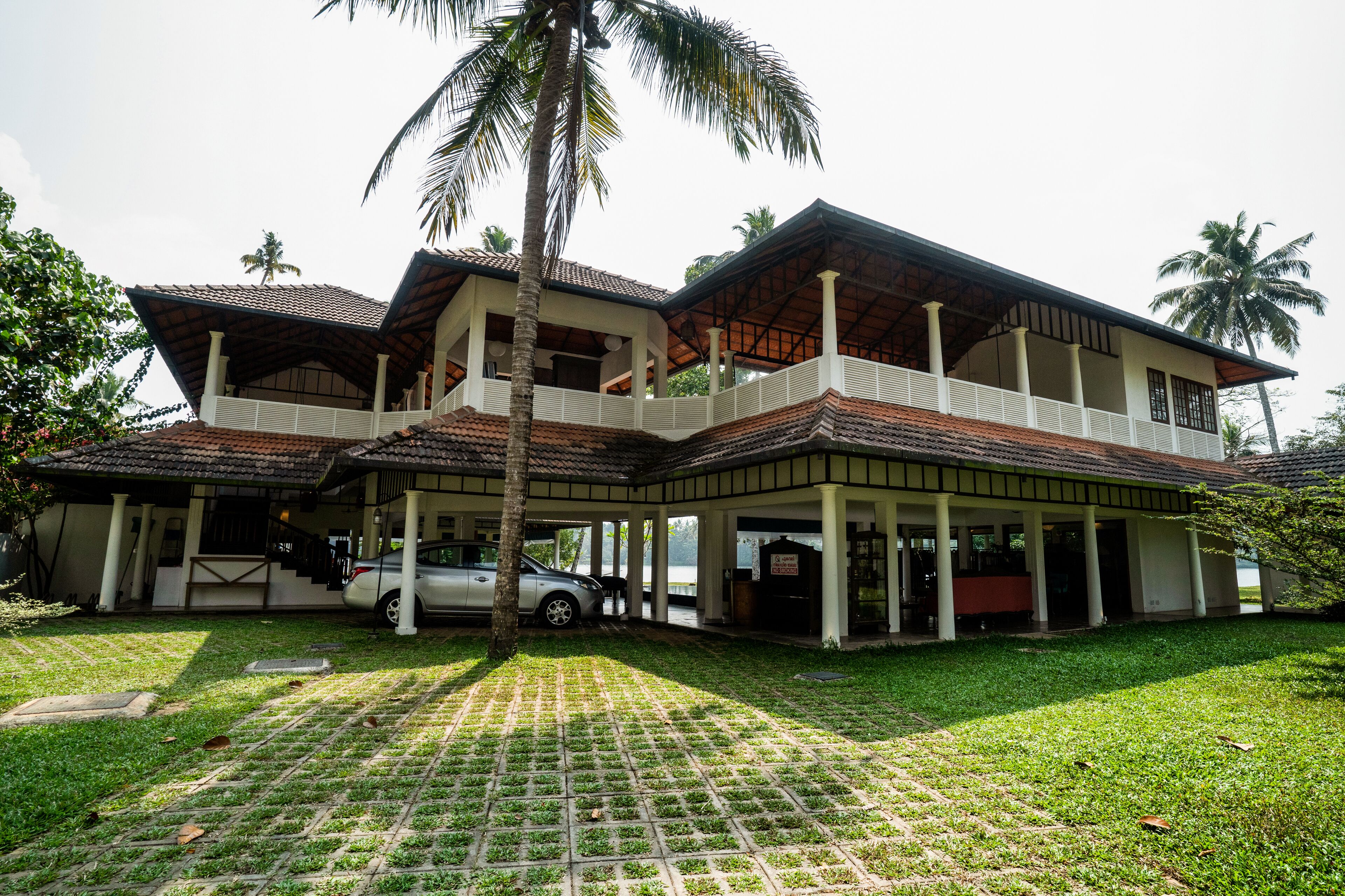 A two-story house with a covered porch, a car parked in front, and a palm tree.